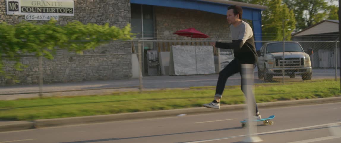 A man rides a blue skateboard on a town road