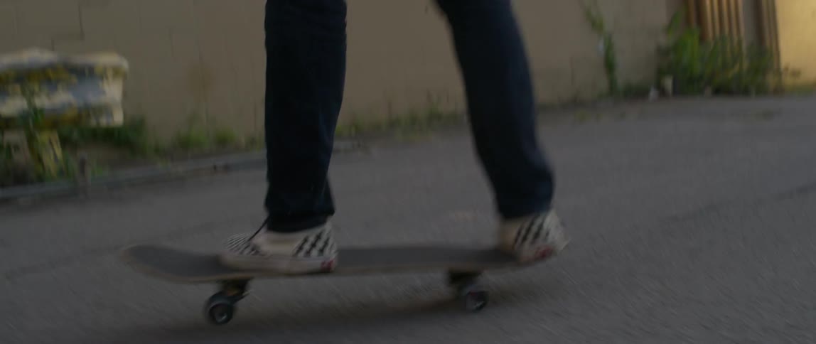 A skateboarder gets on his board and flips it around on asphalt near a building on a sunny day