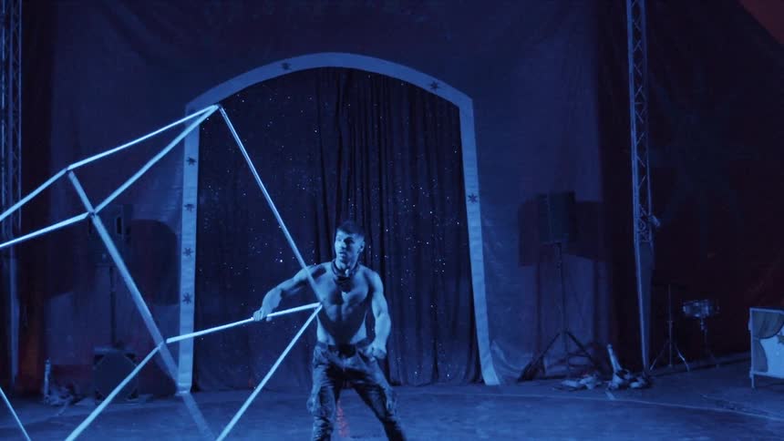 A male performer twirls a giant cubic frame around himself