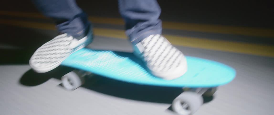 A person wearing checkered shoes rides down a road on a blue skateboard