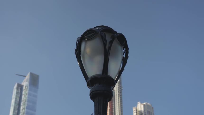 A black iron street lamp with skyscrapers and blue sky behind it