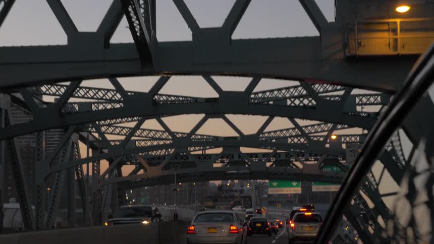 A bridge with beams and signs overhead and many cars driving on it