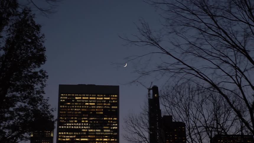 Lights shine through the windows of tall city buildings at dusk