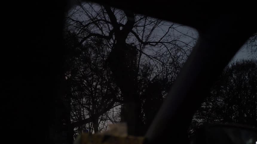 Camera looks out at dark trees and buildings