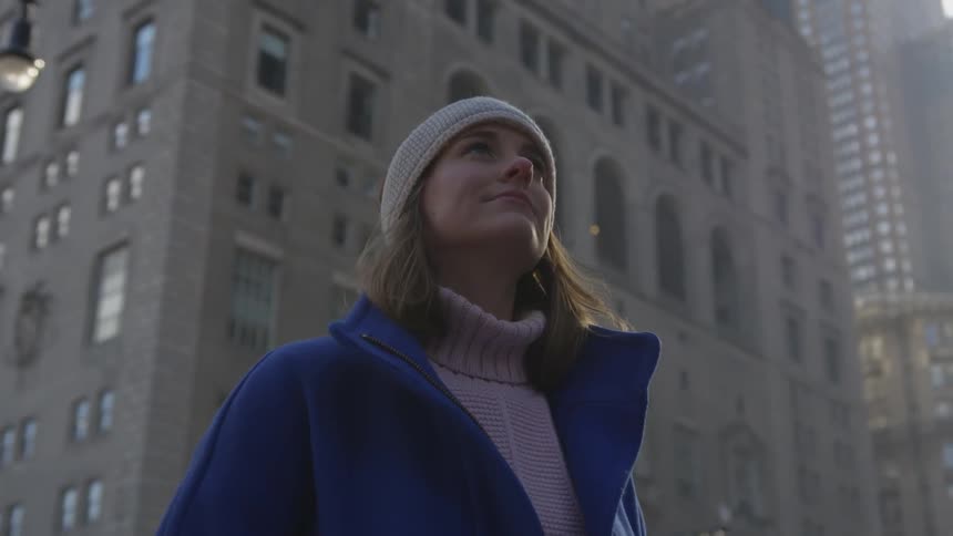A woman in a hat and winter coat standing and staring on a city street