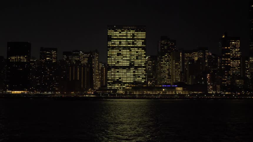A river at night is partly illuminated by a city skyline in which many buildings have lights on