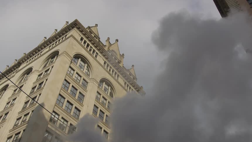 Smoke billows up from street level and a building marked with black char