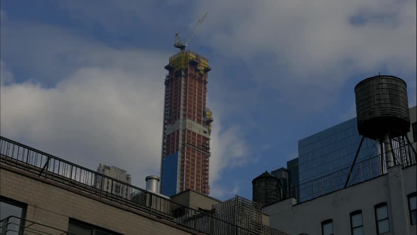 Clouds float over a crane constructing a city skyscraper