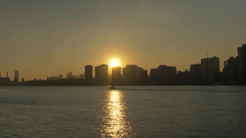 A city skyline at low sun and a boat motoring down a river