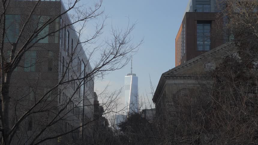 Barren trees in front of a three urban structures with a skyscraper looming in the background