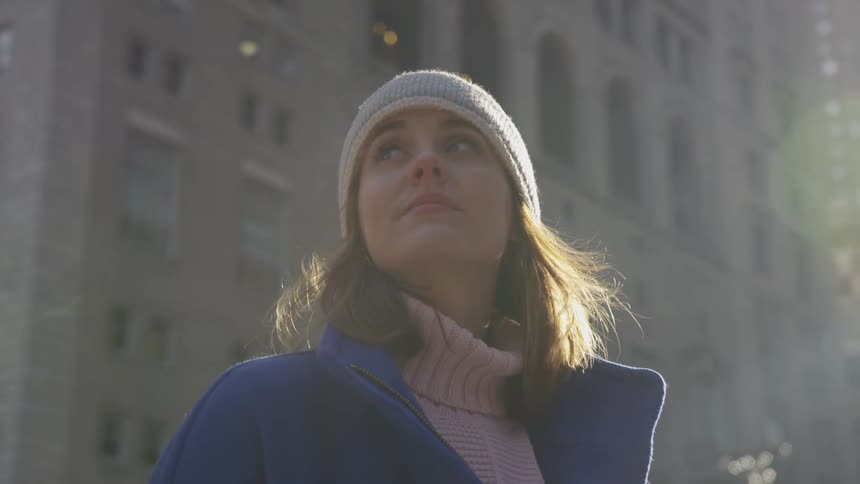 A woman stands in between the buildings while staring upward