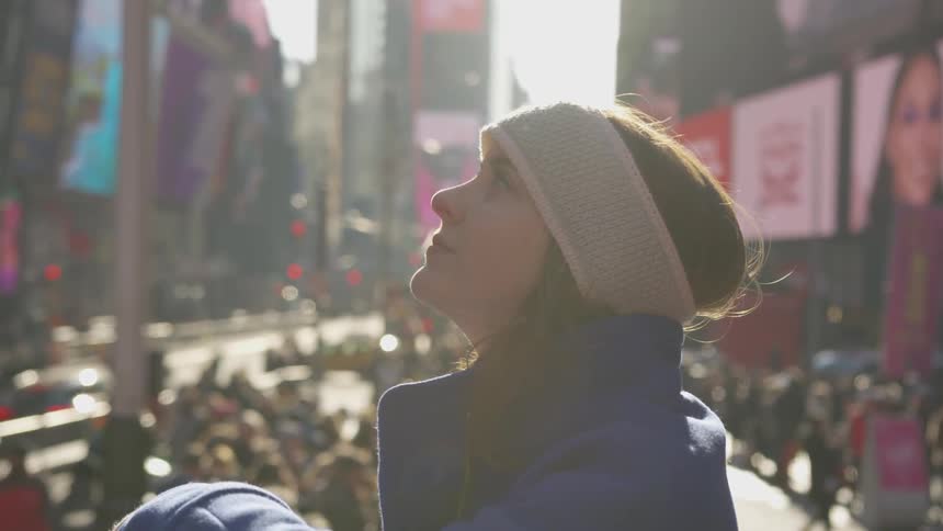 A female wearing a headband and winter coat stands in a busy commercial street