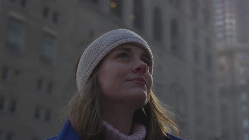 An attractive blond woman wearing a knit cap looks wistfully upwards in the city