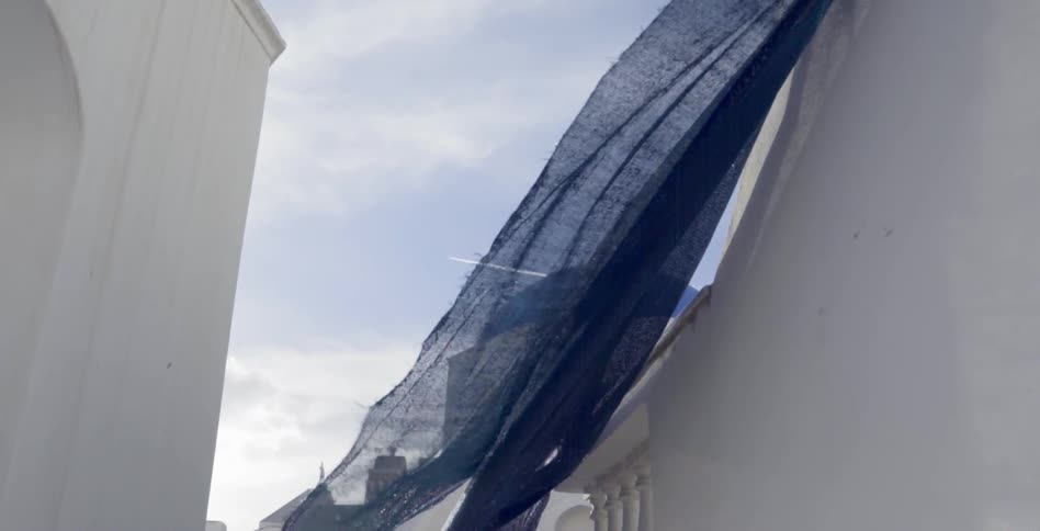 Tattered blue cloth waves from a white wall in the wind