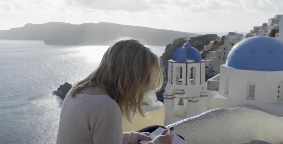 Woman standing on a roof overlooks a body of water as she writes