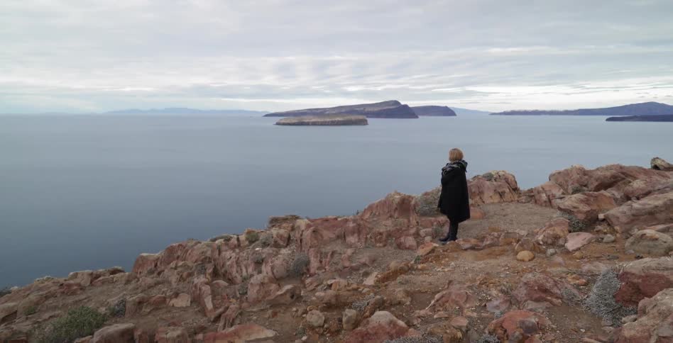 Woman stands on a cliff looking towards the sea