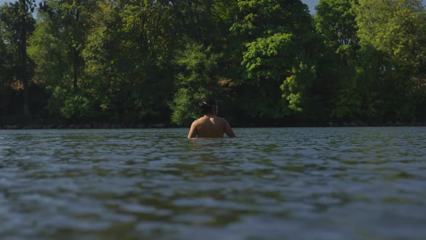 A shirtless man stands waist deep in a flowing river