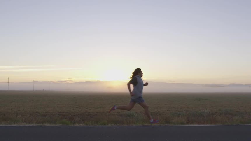 A man jogs on a rural road next to a field at sunrise