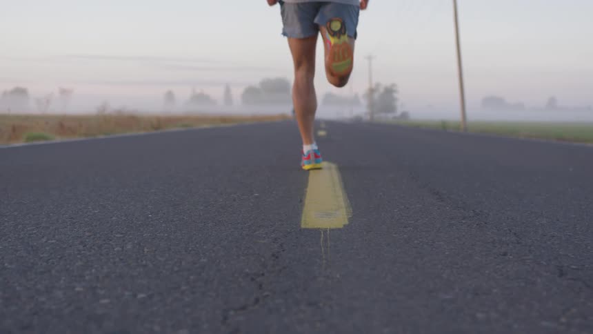 A man in sneakers and athletic shorts runs on a paved road on a foggy day