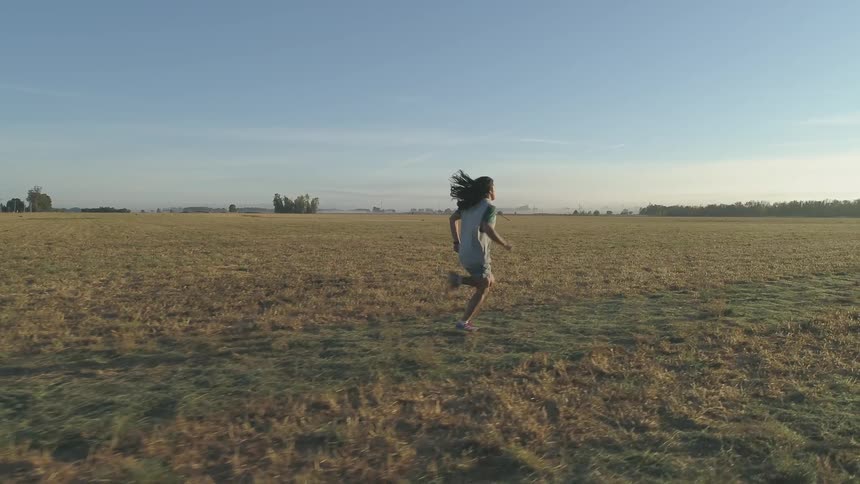 Person with long hair runs through grassland in the daytime