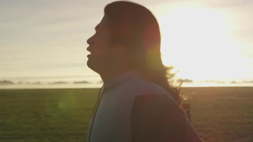 A young man with long black hair runs through a rural area