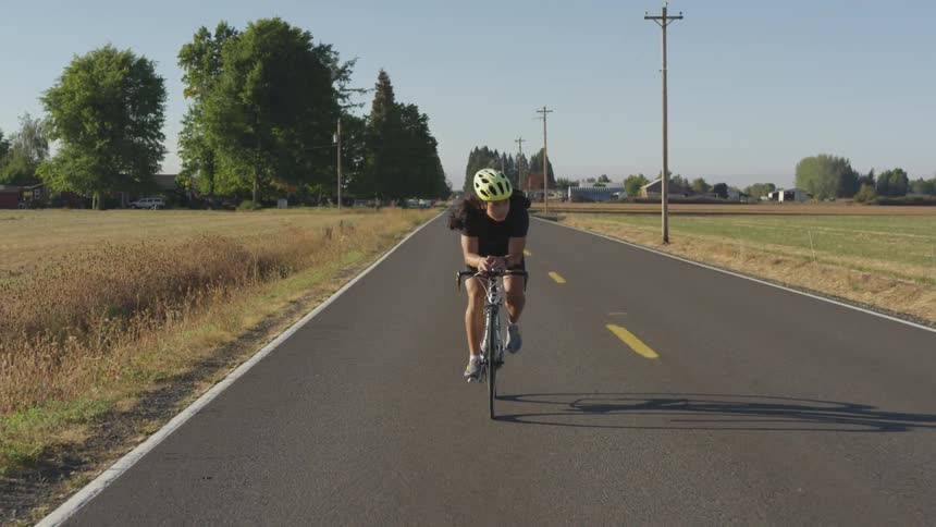 A man cycles on a two lane road while looking over the field