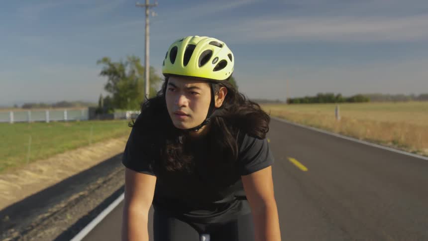 An Asian cyclist cycling down a rural road