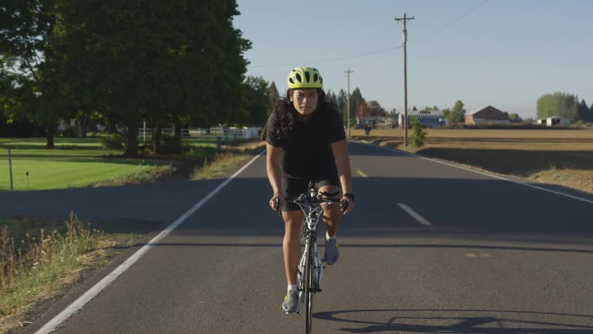 A man rides a bike on a rural two lane road