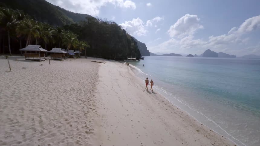 People walk on the beach beside huts on the sand