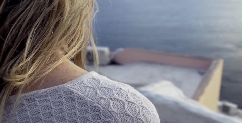 A young woman wearing lace looks out over the ocean from a rooftop