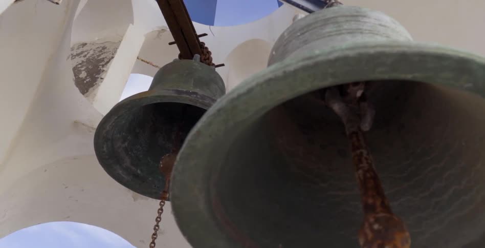Rusty bells hang under a white structure on a sunny day