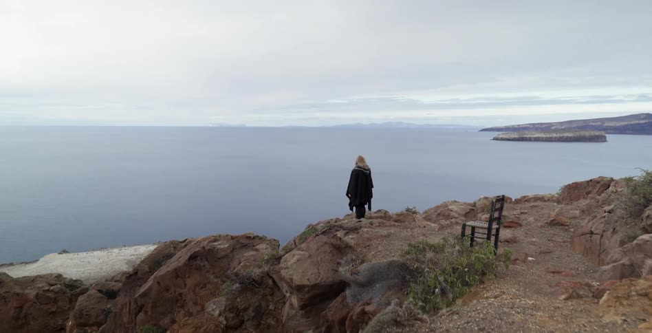 A woman is standing on the edge of a cliff by a body of water