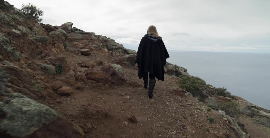 A woman walks on a rocky hill on the coast