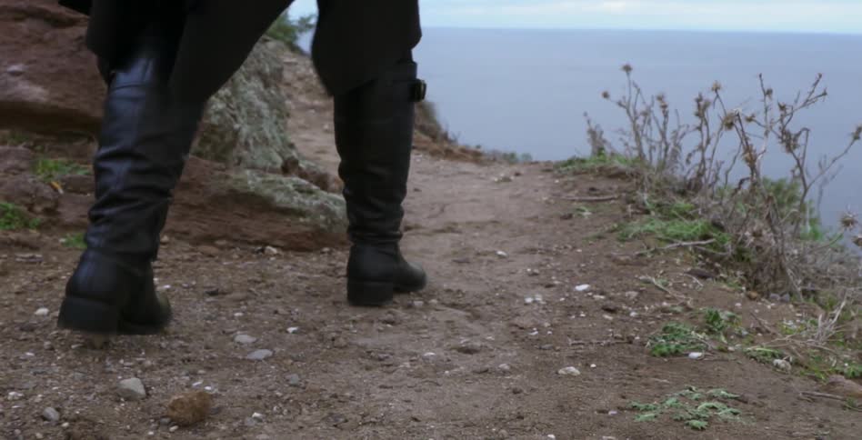 A person wearing tall boots walks in dirt