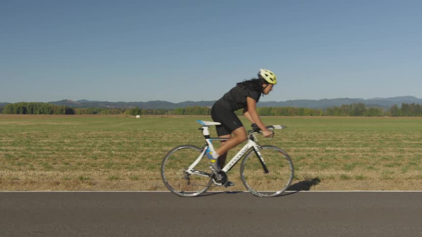A bicyclist with a yellow helmet and black clothing rides down a rural road