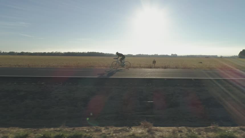 Bicyclist rides down a road between the fields