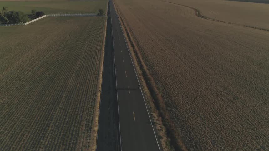 Birds eye view of person biking down freeway surrounded by farmland