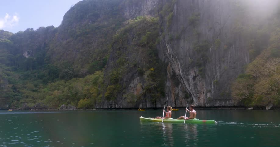 Couple in a two person kayak paddle near a rock face