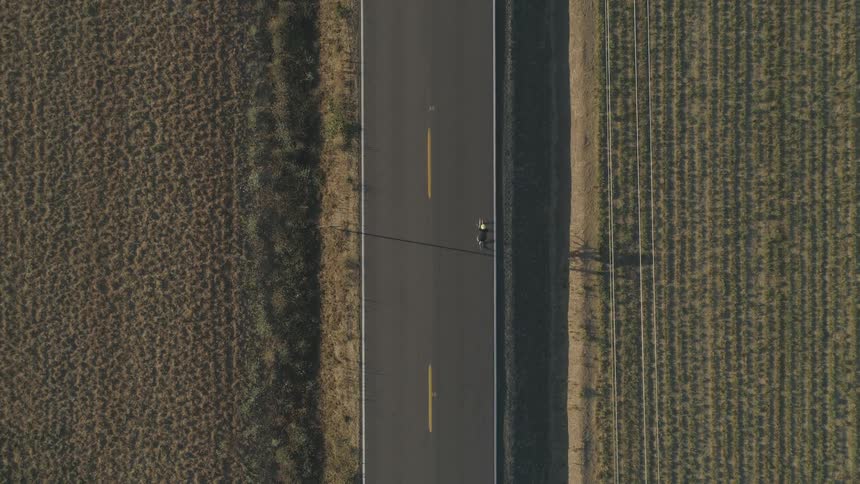 A bicyclist rides down a road that runs through rural farmland
