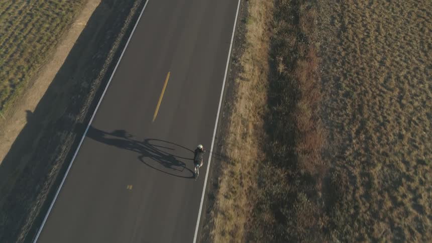 A bicyclist rides a bicycle down a rural road between farm fields