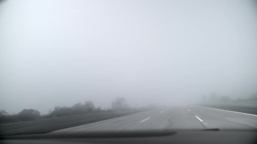 A vehicle driving down a road on a foggy day