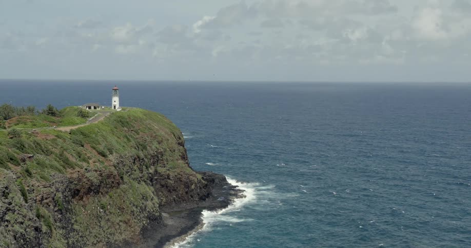 A light tower sits on the side of a steep cliff by the ocean