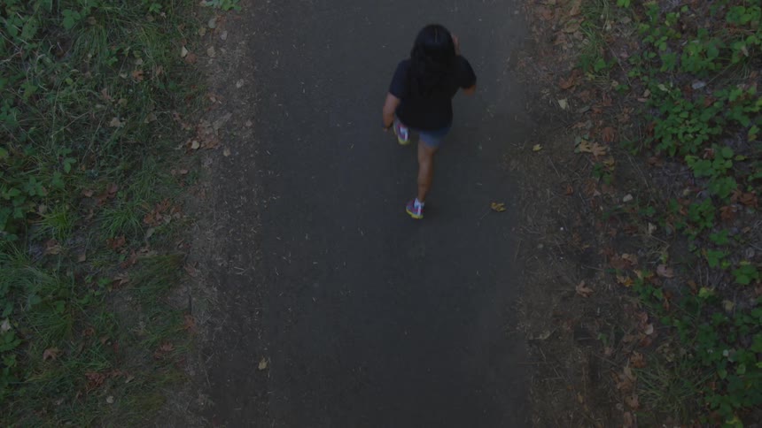 A person with dark hair and jean shorts runs down a narrow path