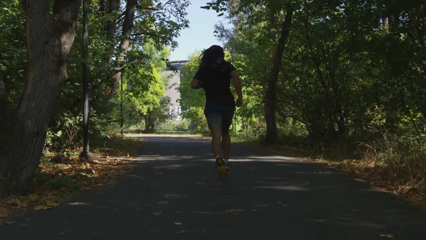 A man with long hair is running on a shaded paved path