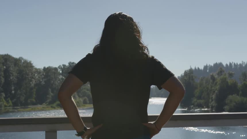 A person stands on a bridge in front of a handrail looking at a river