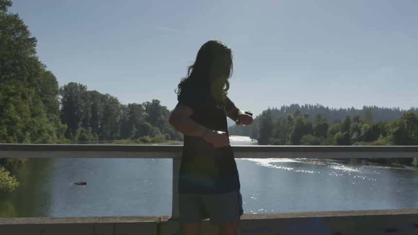 Person exercises on a bridge overlooking a river surrounded by forest on a sunny day
