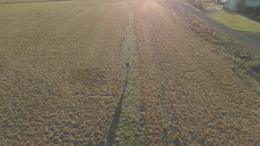 A person is running with great intensity over a open field covered with patchy vegetation in a rural area