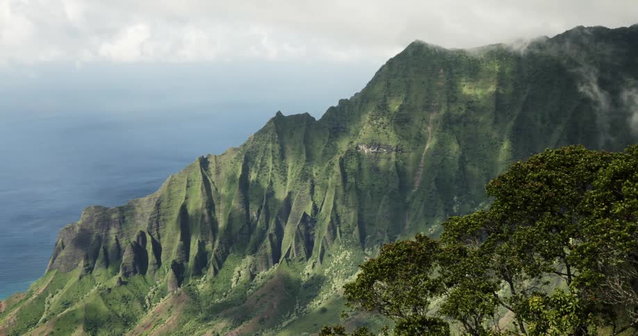 Green lined mountains sit against an ocean backdrop on a cloudy day