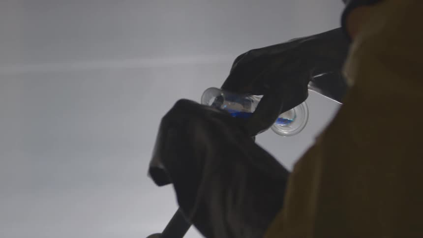 A chemist pours blue liquid from a test tube to another tube as a beaker smokes on the table