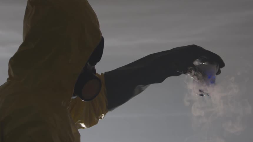 Person in hazmat suit holding a blue smoking liquid in a beaker